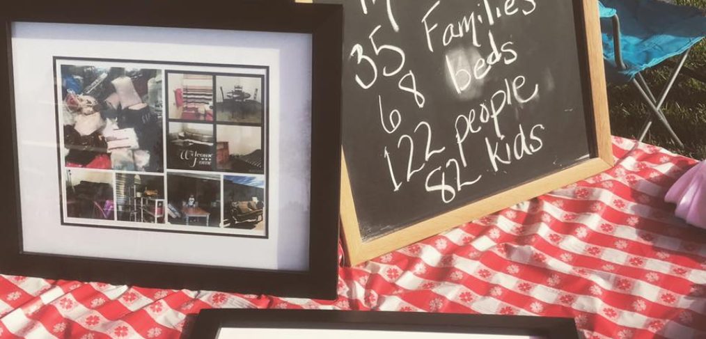 Outdoor display with a chalkboard detailing service stats and framed photos of charity events, set on a picnic blanket.