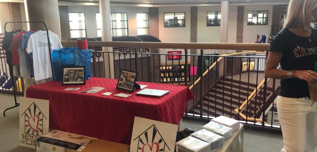 A school merchandise table set up on a balcony with shirts and books for sale, and a person standing beside the table.