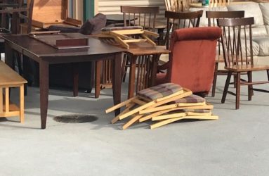 A pile of broken wooden chairs in front of a table inside a room with various other furniture pieces.