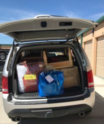 An open suv trunk loaded with various items including boxes, bags, and a disassembled furniture piece, parked outside a storage unit.