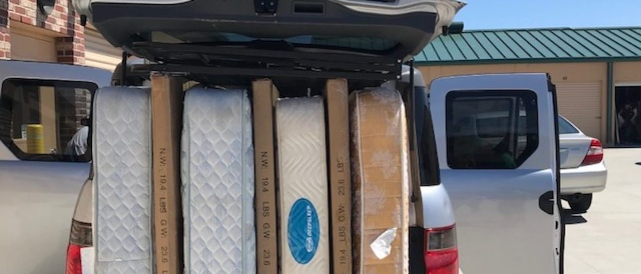 A pickup truck with its tailgate open, loaded with multiple mattresses and box springs, parked at a school.