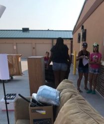 Three people organizing donated items outside a building, likely part of a charitable event or donation drive.