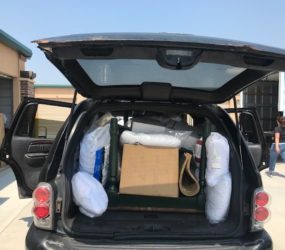 A black suv with an open trunk filled with various items, including bags, boxes, and rolls of insulation, parked in a lot.