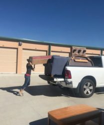 Two people loading furniture into a pickup truck in front of storage units on a sunny day.