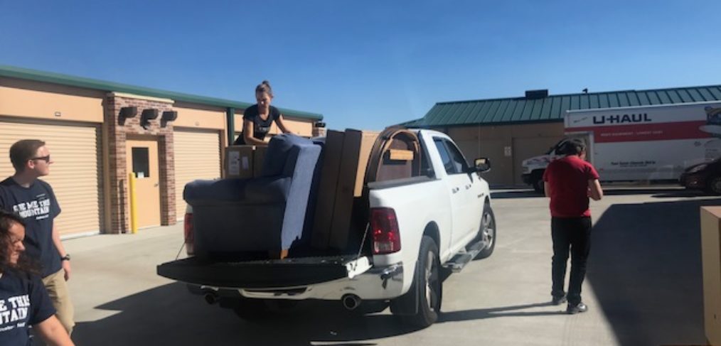 A group of people loading furniture into the bed of a pickup truck in a sunny parking lot.