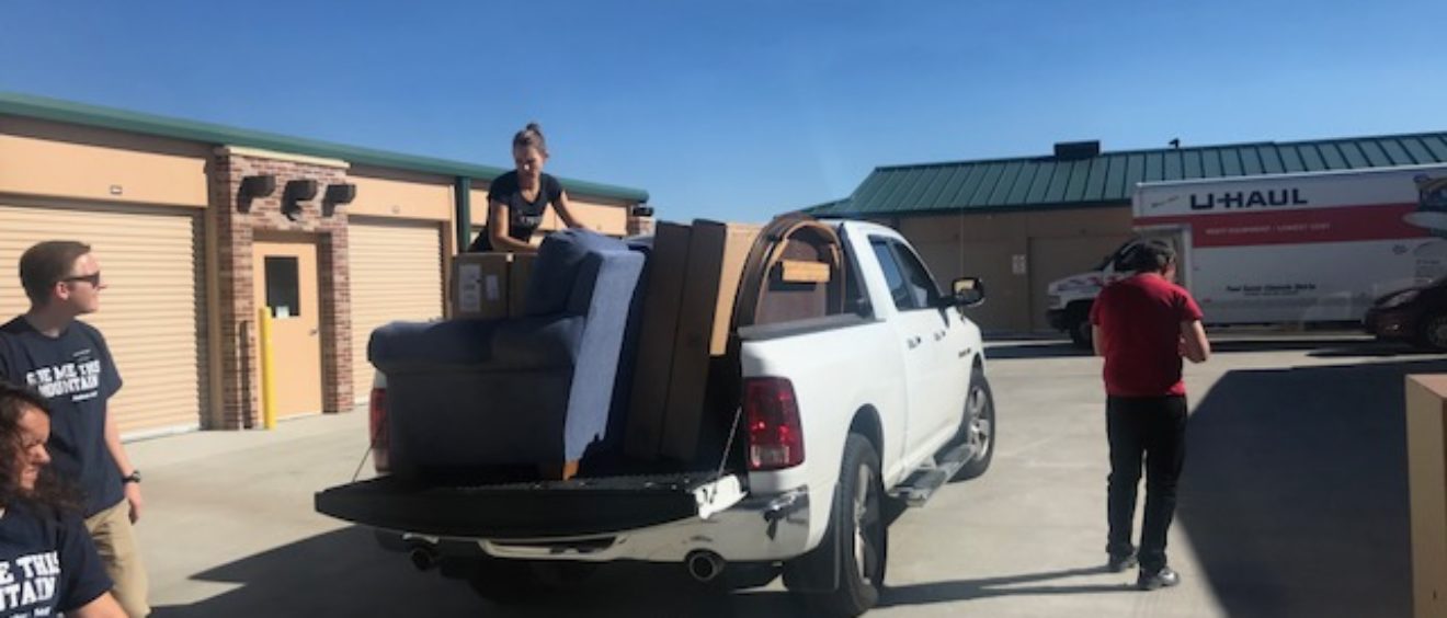 A group of people loading furniture into the bed of a pickup truck in a sunny parking lot.