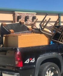 A black chevrolet pickup truck loaded with assorted furniture including chairs and wooden pieces, parked outside storage units.