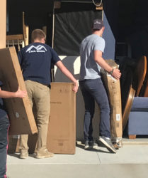 Three people moving boxes and furniture out of a storage unit.