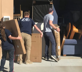 Three people moving boxes and furniture out of a storage unit.