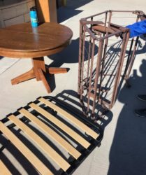 Wooden table and a folding chair with a metal frame on a sunny patio, alongside a blue water bottle.