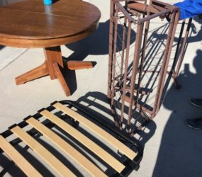 Wooden table and a folding chair with a metal frame on a sunny patio, alongside a blue water bottle.