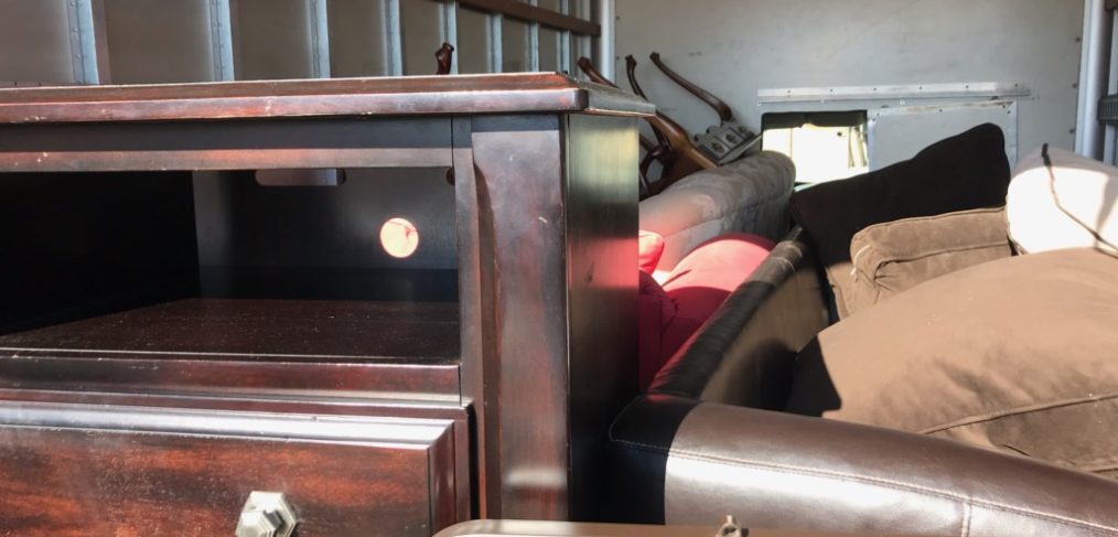 Interior of a moving truck packed with various furniture items including a wooden cabinet, mattresses, and a disassembled bed frame.