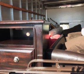 Interior of a moving truck packed with various furniture items including a wooden cabinet, mattresses, and a disassembled bed frame.