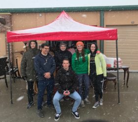 Group of six people smiling under a red and white tent in a snowy environment.