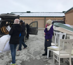 People loading chairs and other items into a car in a parking lot on a cloudy day.