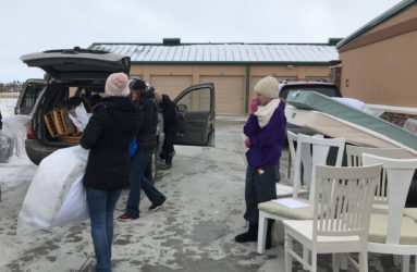 People loading chairs and other items into a car in a parking lot on a cloudy day.