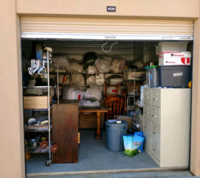 Open garage storage unit filled with various items including furniture, boxes, and bins.