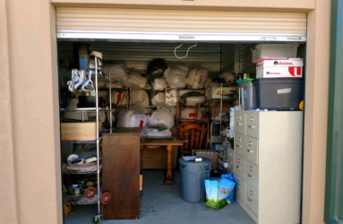 Open garage storage unit filled with various items including furniture, boxes, and bins.