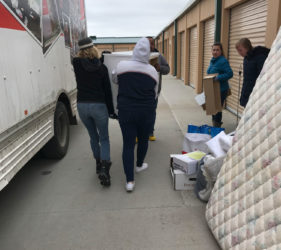 People loading large items and boxes into a truck at a storage facility.
