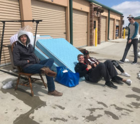 Two people relaxing on furniture outside a storage facility, with a third person standing in the background. snow is visible on the ground.