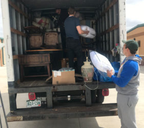 Two men loading furniture and boxes into the back of a moving truck while another man watches.