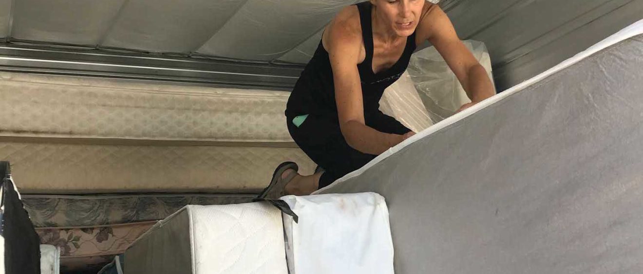 A woman climbing over stacked mattresses in a storage area.