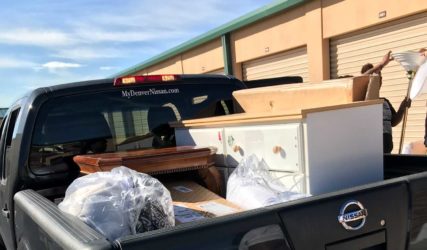 A pickup truck loaded with assorted items such as furniture and bags, parked outside a storage facility under a clear blue sky.