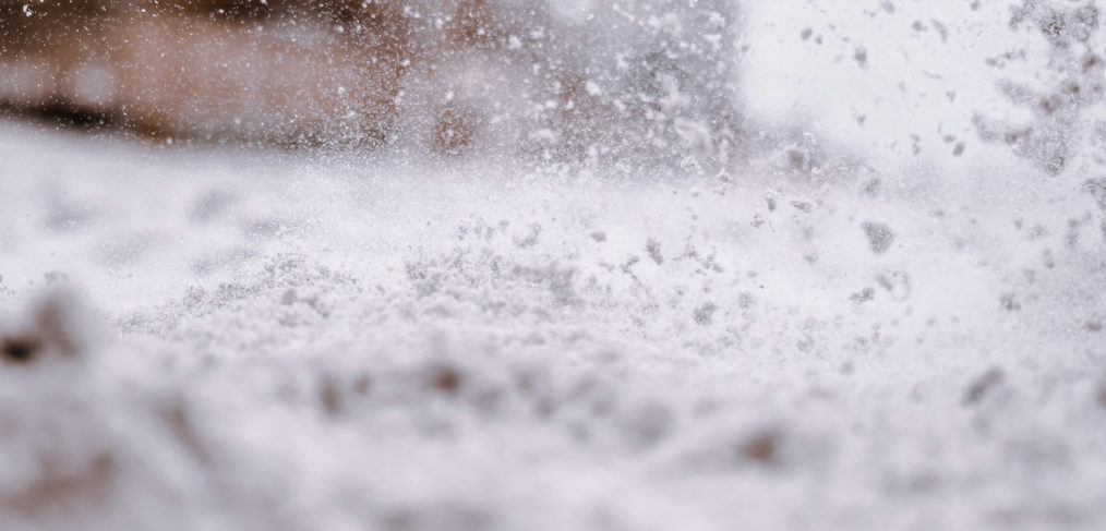 Close-up of snow particles flying through the air during a snowstorm, with a blurred background.