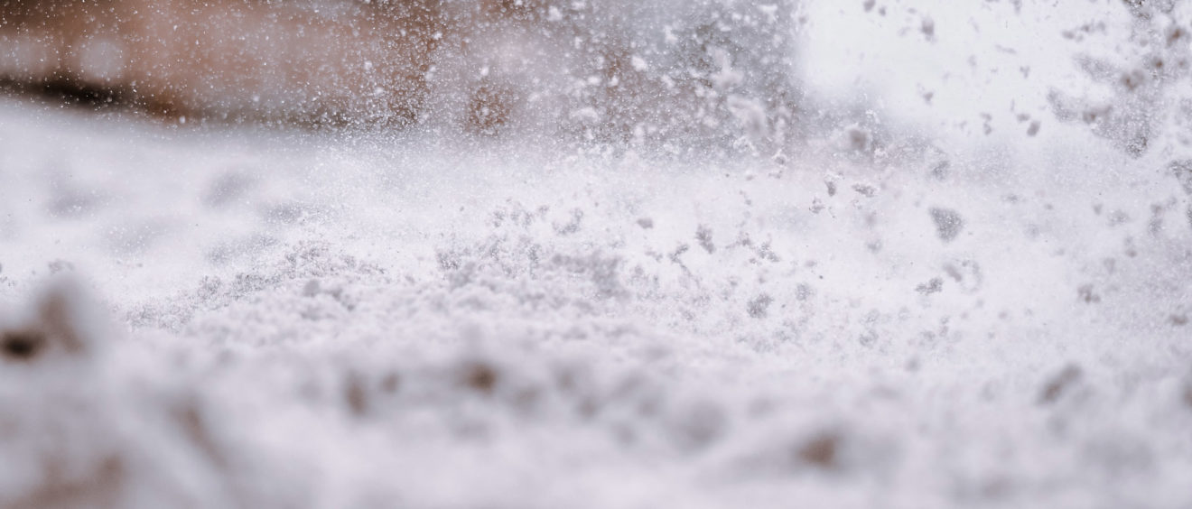 Close-up of snow particles flying through the air during a snowstorm, with a blurred background.
