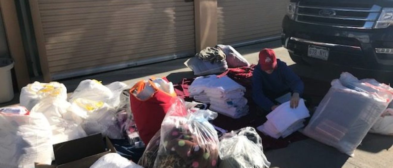 Person sorts through various items next to a parked car in front of an open storage unit under bright sunlight.