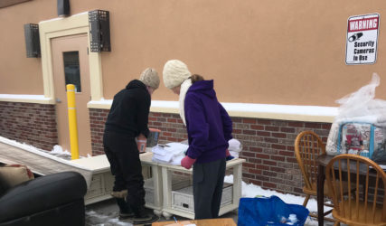 Two people standing outside of a building with furniture.