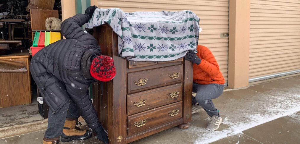 Two people are hiding behind a dresser.