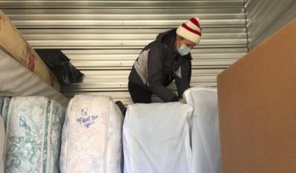 A man is standing on top of mattresses in a storage unit.