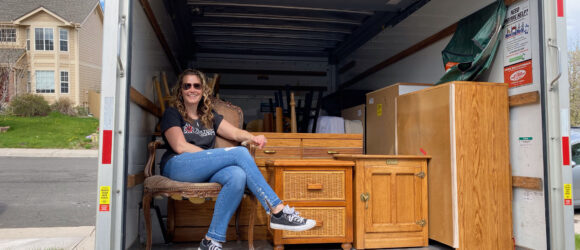 A woman sitting on the back of a moving truck.