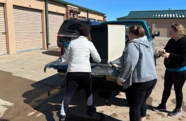 Three women loading a refrigerator into the back of a truck.