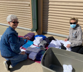 Two women sitting on the ground with a large amount of clothes.