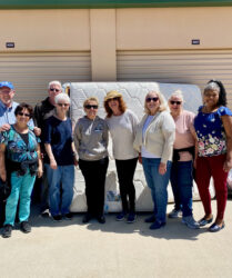 A group of people standing next to a mattress.