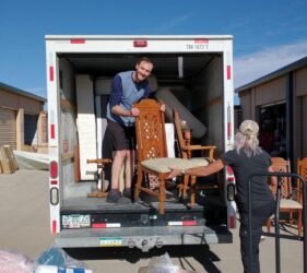 A man and woman loading furniture into the back of a truck.