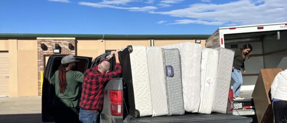 A man and woman loading mattresses into the back of a truck.
